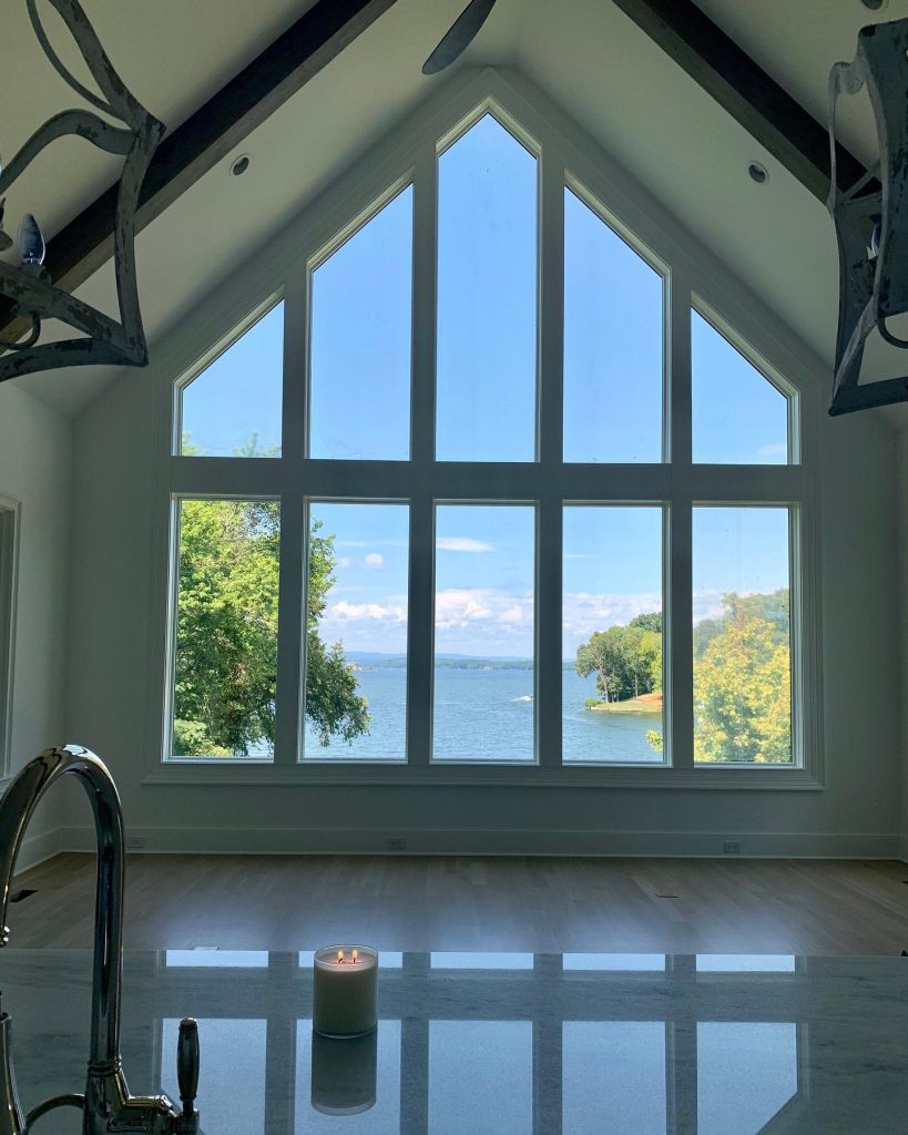 Large triangular window with a scenic view of a lake and greenery from inside a modern home